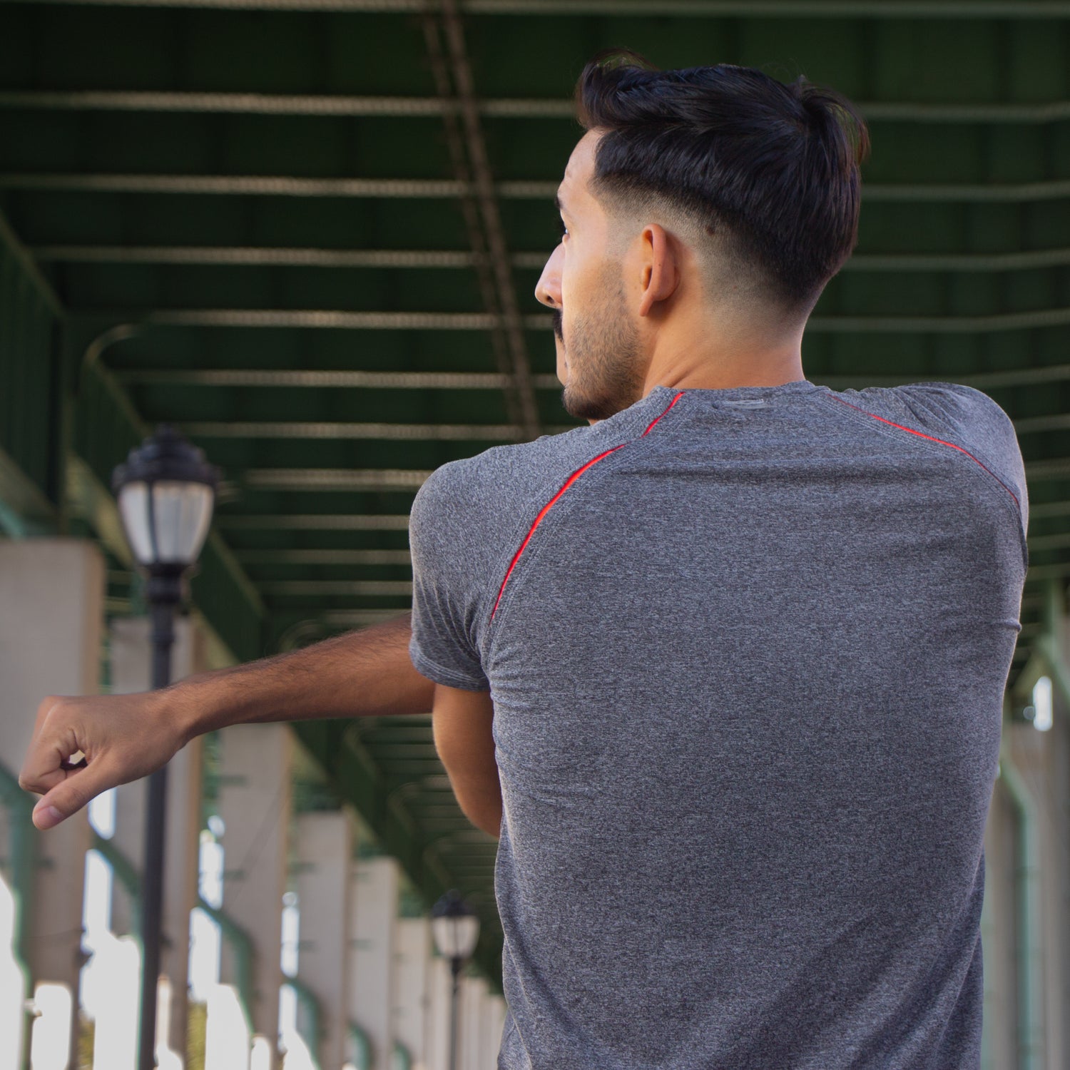 A man stretches his arms from the back wearing a charcoal shirt with persimmon colored accents peeping through.