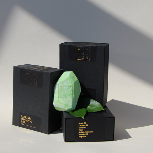 A green shampoo bar and leaves on black and gold paper boxes