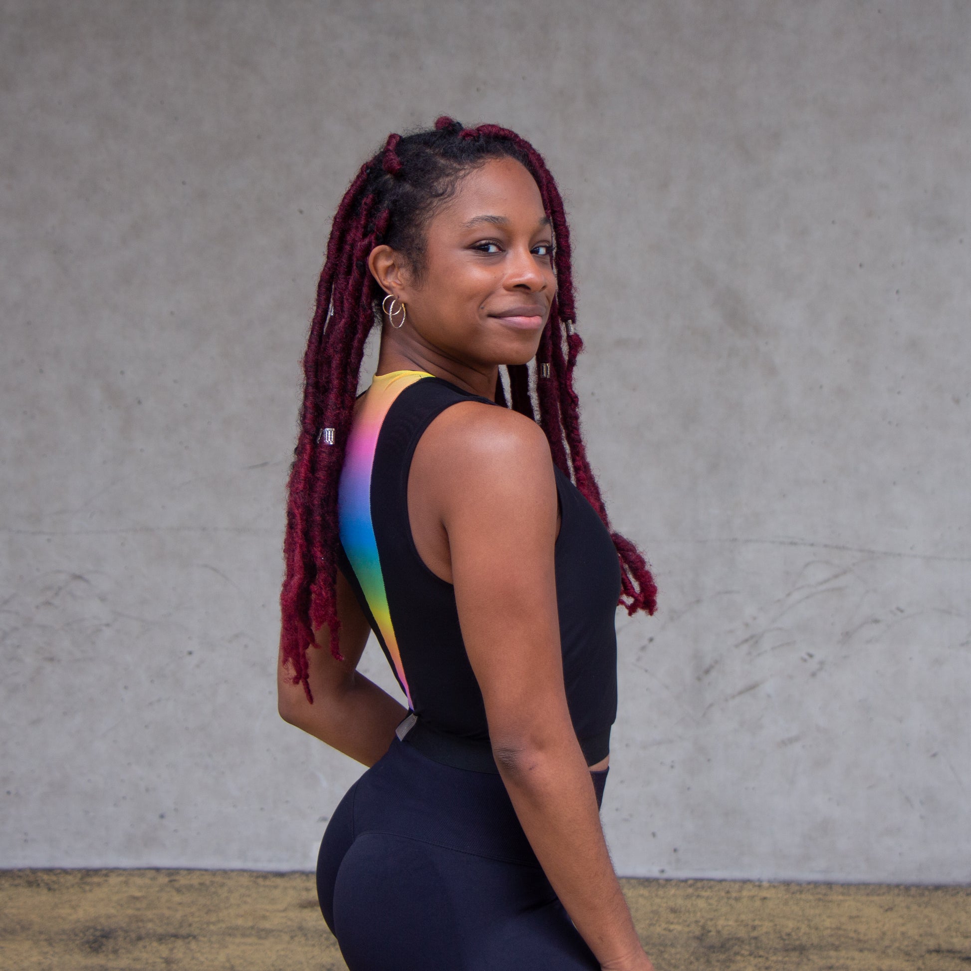 a photo of a black woman looking over her shoulder wearing a black croptop with rainbow accents 