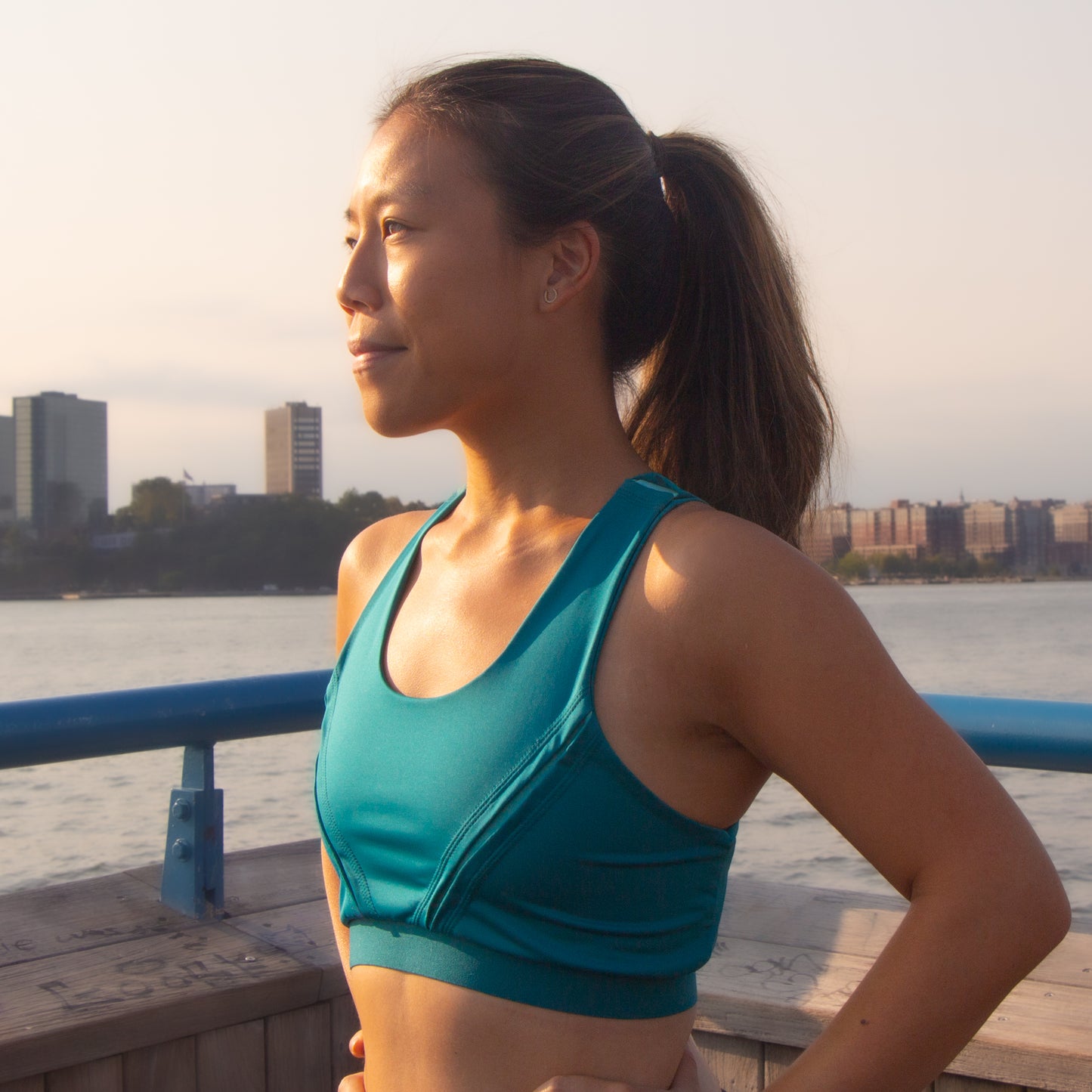 A photo of an east asian woman looking into the sun wearing a teal and mint sports bra