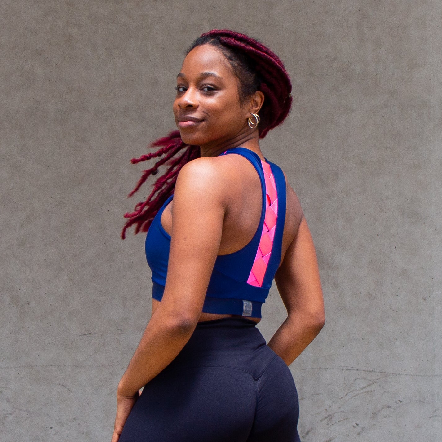 a photo of a black woman flipping her hair while wearing a blue and pink sports bra with a woven elastic detail